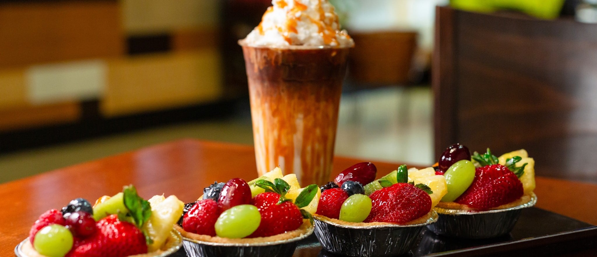 A line of assorted fresh fruit tarts and a caramel coffee drink with whipped cream